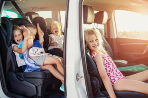 Des enfants souriants à l'intérieur d'une voiture, impatients de partir au camping, entourés de sacs de voyage et d'équipements de plein air. L'image évoque l'excitation d'une aventure en famille en pleine nature.